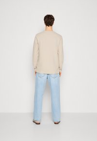 Beige långärmad skjorta med rund halsringning, tillsammans med ljusblå vida jeans. Slät textur, minimal detaljering och en avslappnad passform.