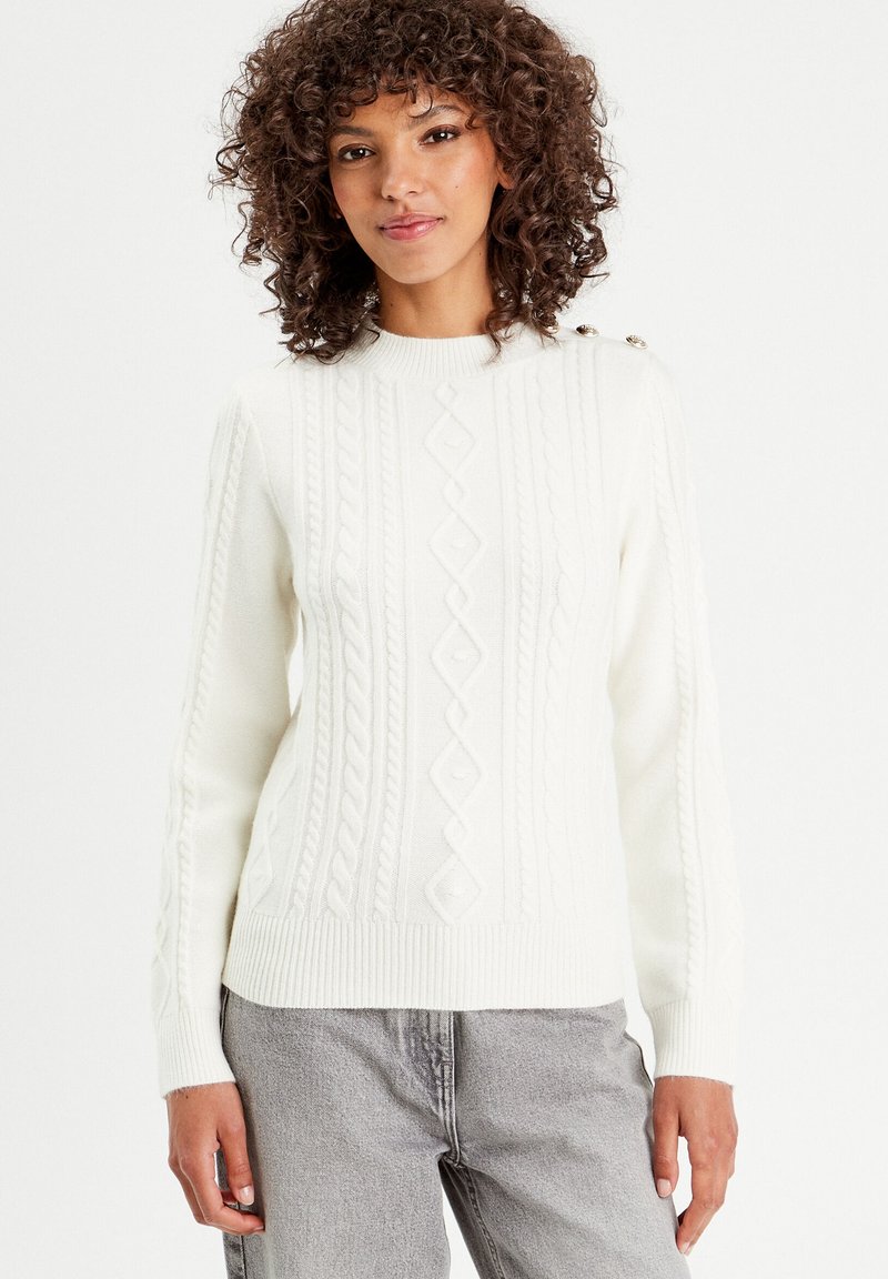 Pull en maille blanc avec motif en cable, encolure ronde et trois boutons décoratifs à l'épaule. Texture douce et coupe ajustée.