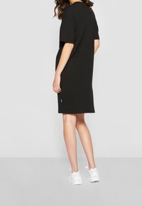 Czarna bawełniana sukienka T-shirt z krótkim rękawem, luźny krój i długość do kolan. W połączeniu z białymi sportowymi sneakersami. Minimalistyczne detale.