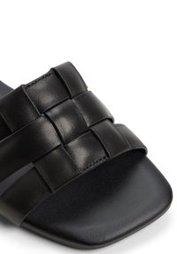 Svarta lädersandaler med platt sula, med ett flätat remdesign, fyrkantig tå och en slät botten. Accentueras av subtila stygn.