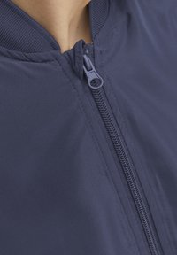 Granatowa kurtka bombowa z gładkim wykończeniem, z zamkiem błyskawicznym z przodu oraz prążkowanym kołnierzem dla większego komfortu i stylu.