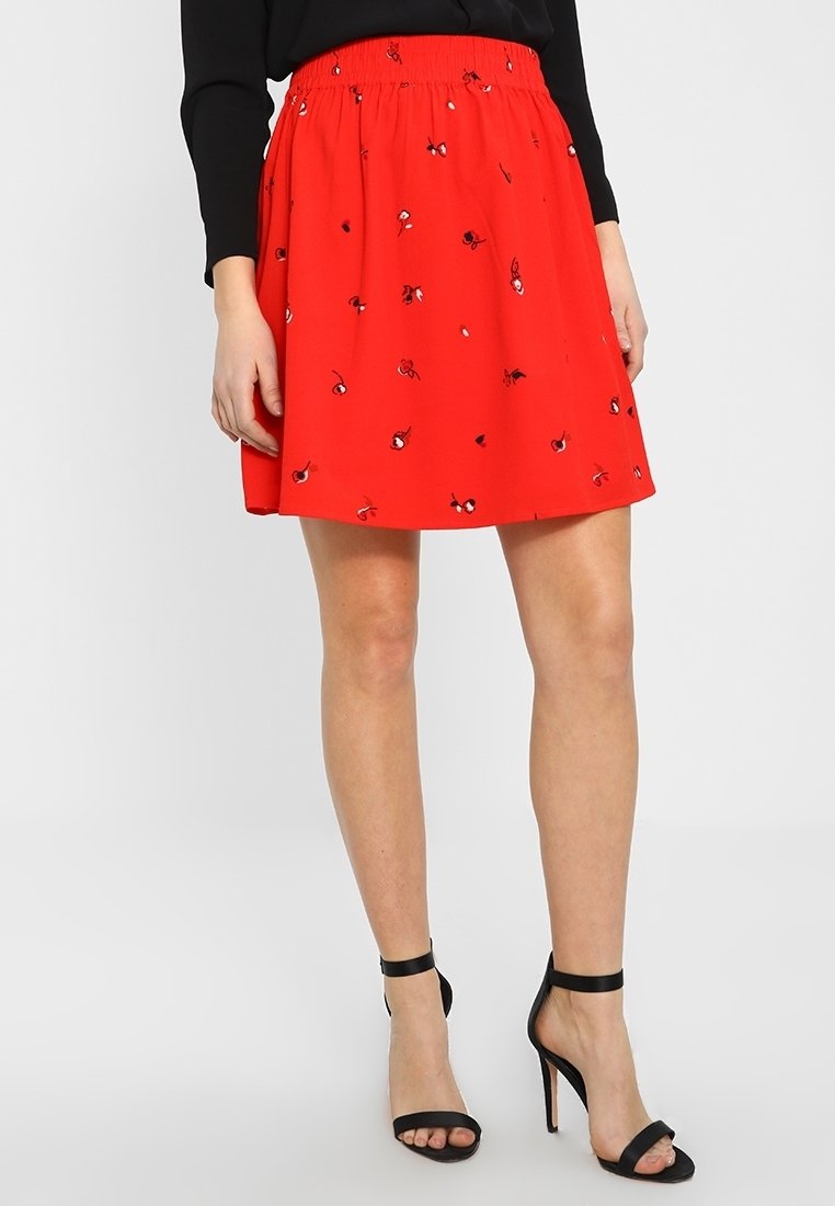 Jupe rouge avec taille élastique, ornée de broderies florales noires dispersées, longueur genou, et tissu léger.