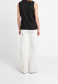 Haut noir sans manches associé à un pantalon blanc ample. Tissu lisse, coupe décontractée et jambes larges mettant en valeur la simplicité.