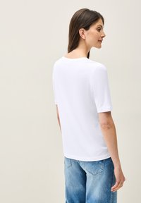 Bílý krémový T-shirt s krátkým rukávem, kulatým výstřihem, jemnou texturou a volným střihem, doplněný o světle modré džíny.