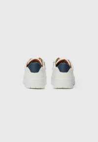 Weiße Sneaker mit einem blauen Fersenakzent, glatter Textur und einer dicken Sohle. Verfügt über dezentes Branding an der Ferse. Rückansicht gezeigt.