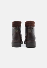 Barna bőr bokacsizmák steppelt mintával, puha barna lehajtható szegéllyel, barázdált gumitalppal és díszes fém kiegészítőkkel.