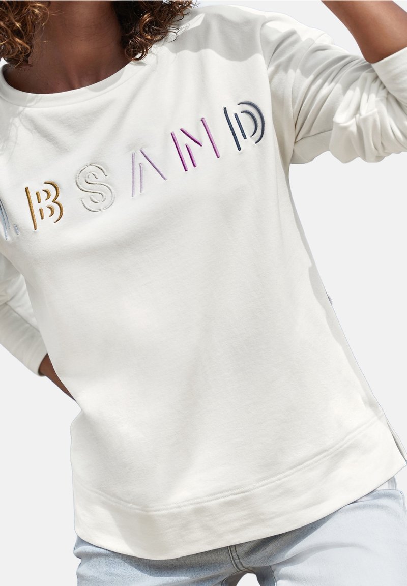 Sudadera crema con texto bordado en relieve y colorido que dice "ABSAND" en la parte frontal. Fabricada en un material suave con un corte relajado y puños acanalados.