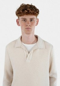 Stickad pullover i ljus krämfärg, med ett diamantmönster och en spetsig krage, utrustad med långa ärmar och en avslappnad passform.