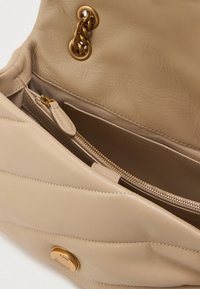 Beige bőr kézitáska, textúrált felülettel, aranylánc díszítéssel és cipzáros belső zsebbel a biztonságos tárolás érdekében.