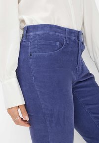 Lilla corduroy bukser med høj talje, der har frontlommer og en tekstureret overflade. Sammen med en hvid bluse.