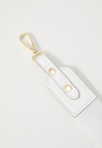 Cinturino bianco con dettagli in pelle texturizzata, clip in metallo dorato e due bottoni a pressione circolari, progettato per fissare gli accessori in modo sicuro.