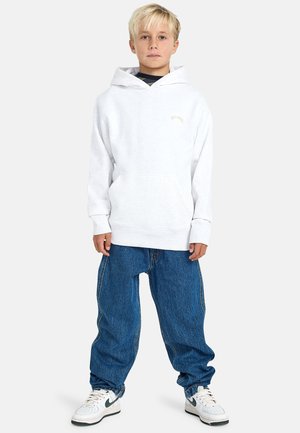 Lichtgrijze hoodie met een voorzak, gecombineerd met baggy blauwe spijkerbroek en witte sneakers met groene accenten.