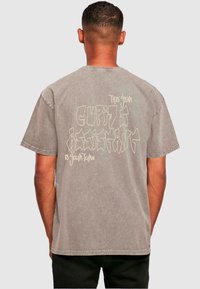 Grå kortærmet t-shirt med en afslappet pasform. Har et abstrakt tekstdesign i lysere farve på ryggen. Lavet af bomuldsstof med en blød tekstur.