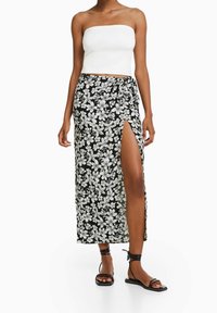 Černá maxi sukně s květinovým vzorem, která má rozparek až ke stehnům, lehký materiál a zavinovací design. V kombinaci s bílým topem bez ramínek a černými sandály.