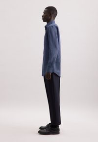 Navy button-up shirt met een geometrisch stippenpatroon, gecombineerd met op maat gemaakte zwarte broeken en zwarte schoenen. Zijaanzicht vangt de pasvorm en het ontwerp.