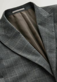 Grau karierter Blazer mit Reverskragen, der ein strukturiertes braunes Futter zeigt. Besitzt eine taillierte Passform mit definierten Schultern.