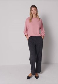 Vaaleanpunainen pitkähihaisen paita, jonka hihat on käännetty, yhdistetty tummanharmaisiin leveälahkeisiin housuihin. Mustat teräväkärkiset tasapohjaiset kengät täydentävät asun.