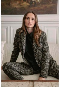 Blazer et pantalon en imprimé léopard dans des nuances de marron et de noir. Le tissu a une texture lisse, avec une coupe ajustée et des revers nets.
