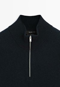 Donkerblauwe wollen pullover met een hoge kraag en een zilveren rits. Geribbeld textuur bij de kraag. Etiket zegt "Massimo Dutti" en "100% wol."