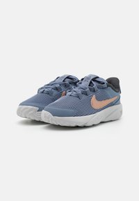 Baskets Nike avec un dessus en textile bleu à côtes, un logo doré rose et une semelle en caoutchouc texturé blanche. Fermeture à lacets avec col rembourré.