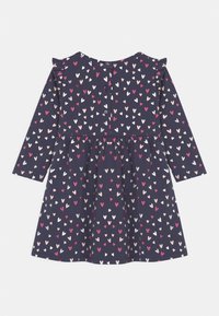 Tmavě modré šaty s dlouhými rukávy, ozdobné volánky a zapínáním na knoflíky. Vyznačují se vzorem malých barevných srdíček v růžové, bílé a červené barvě.