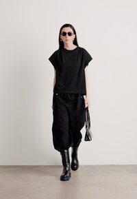Černé oversized tričko s krátkým rukávem, volné černé kalhoty a černé kozačky po kolena. Mezi doplňky patří černé sluneční brýle a malá kabelka.