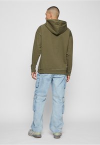 Oliva roheline kapuutsiga pusa, millel on paindlik istuvus, soonikkoes varrukaotsad ja sileda tekstuuriga kangas. Kandmiseks on valitud helesinised cargo-püksid.