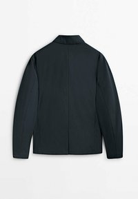 Giacca verde scuro con colletto, maniche lunghe, cuciture minime e tasche laterali, caratterizzata da una texture liscia e un design affusolato.