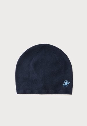 Mørkeblå strikket hue med et lille lyseblåt broderet logo nederst til højre på en ensfarvet lys baggrund.