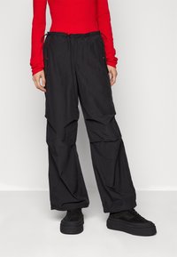 Pantaloni neri, leggeri e larghi con vita elastica e cordoncino, dotati di tasche laterali e una finitura testurizzata.