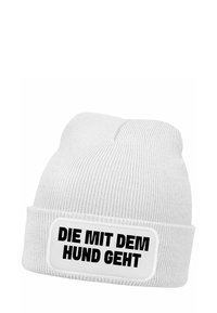 White knit beanie with a folded cuff, featuring a rectangular label with bold black text that reads "DIE MIT DEM HUND GEHT."