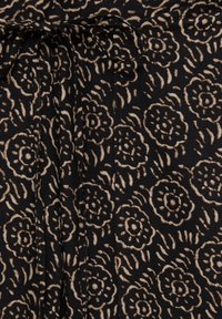 Tissu noir avec un motif floral beige, doté d'un détail de taille nouée. Le design comprend des fleurs texturées et complexes avec des centres circulaires.