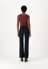 Top de tirantes burdeos ajustado combinado con pantalones de pierna ancha de talle alto en color navy. Los pantalones cuentan con bolsillos traseros y una textura suave. Sandalias negras de tacón.