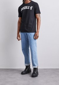 Černé bavlněné tričko s textem "DOUBLE" v bílé barvě, spárované se světle modrými džínami, s ohrnutými rukávy a černými šněrovacími botami.