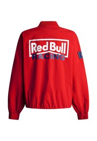 Chaqueta roja con el logo "Red Bull Racing" en blanco y azul en la parte trasera y un pequeño parche con logo en la manga derecha, puños y cinturilla elásticos.