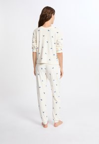 Conjunto de loungewear de algodón blanco que incluye un cuello redondo y mangas largas, con un estampado de lazo azul marino en todo el conjunto y puños ajustados en los pantalones.