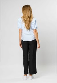 Light blue short-sleeve blouse with puffed sleeves, black wide-leg pants, and white sneakers. Hair is long and straight, falling past the shoulders.