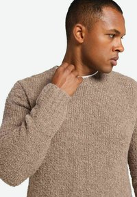 Beżowy sweter dzianinowy o fakturowanym wykończeniu, z długimi rękawami i okrągłym dekoltem, noszony przez mężczyznę patrzącego na bok.