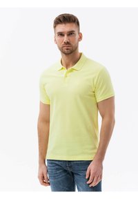 Keltainen polo-paita, jossa on klassinen kaulus, lyhyet hihat ja teksturoitu kangas. Paidassa on pieni logo rintaan ja slim fit -leikkaus.
