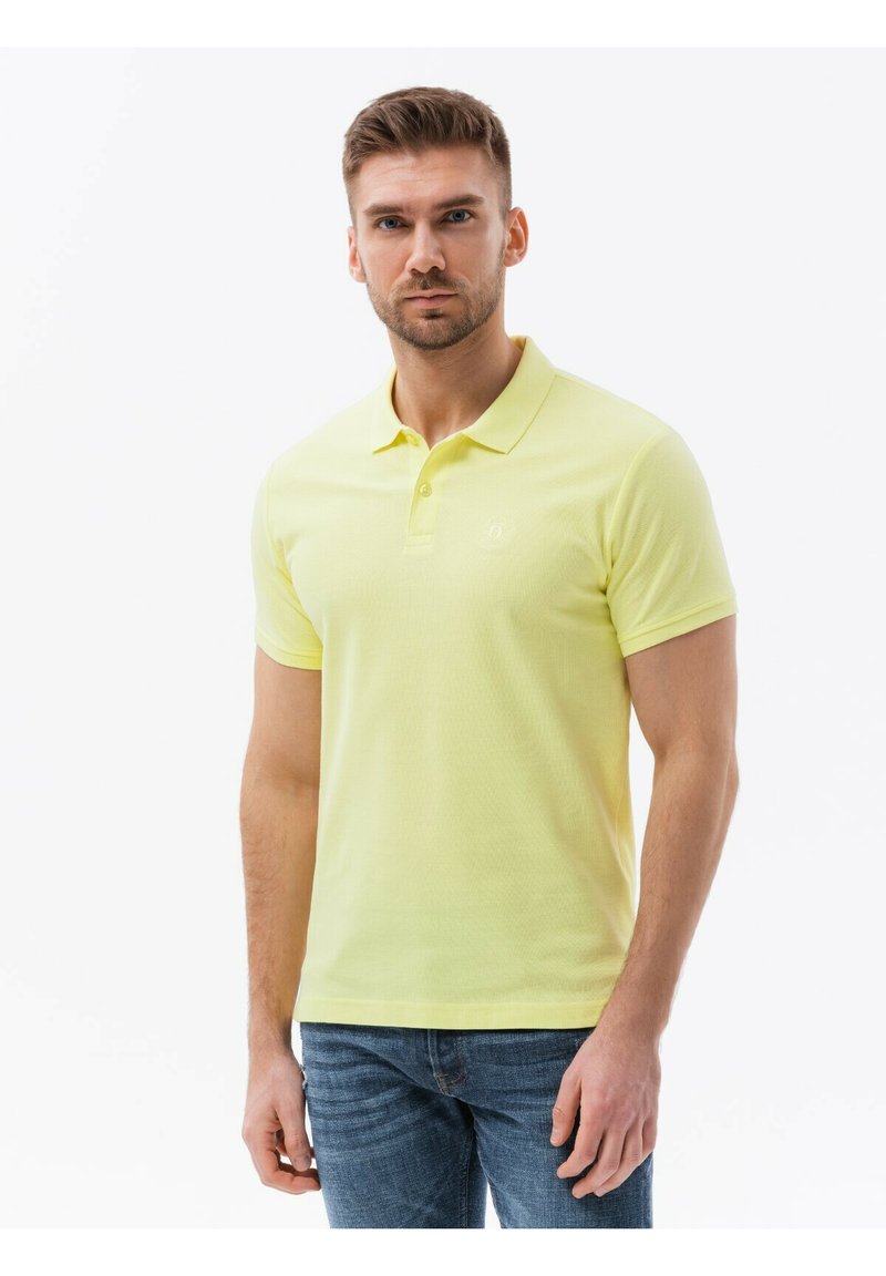 Keltainen polo-paita, jossa on klassinen kaulus, lyhyet hihat ja teksturoitu kangas. Paidassa on pieni logo rintaan ja slim fit -leikkaus.