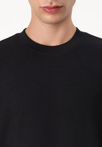 Pull noir à côtes avec un col rond, présentant un tissu texturé et une coupe ajustée. Aucun motif distinct ni détail supplémentaire visible.