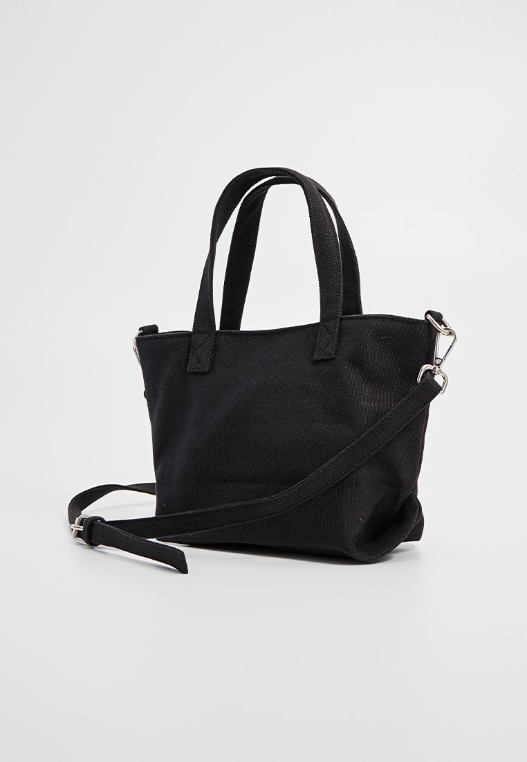 Sac fourre-tout noir en toile avec deux poignées courtes et une bandoulière amovible, présentant une texture lisse et un design minimaliste.