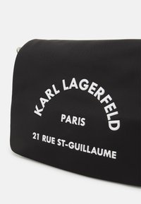 Czarna tkaninowa torba z białym napisem "KARL LAGERFELD PARIS" oraz "21 RUE ST-GUILLAUME". Gładka tekstura i zaokrąglony kształt.