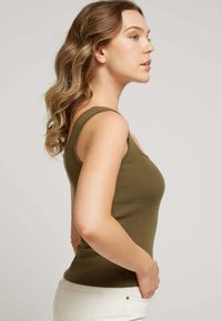 Débardeur en vert olive, côtelé, avec un décolleté arrondi et des bretelles larges, au design ajusté et à la texture douce, associé à un pantalon de couleur claire.