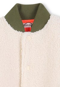 Giacca in pile color crema con colletto a coste verde oliva, dotata di chiusura a scatto e foderata in un vivace arancione. Materiale morbido e strutturato.