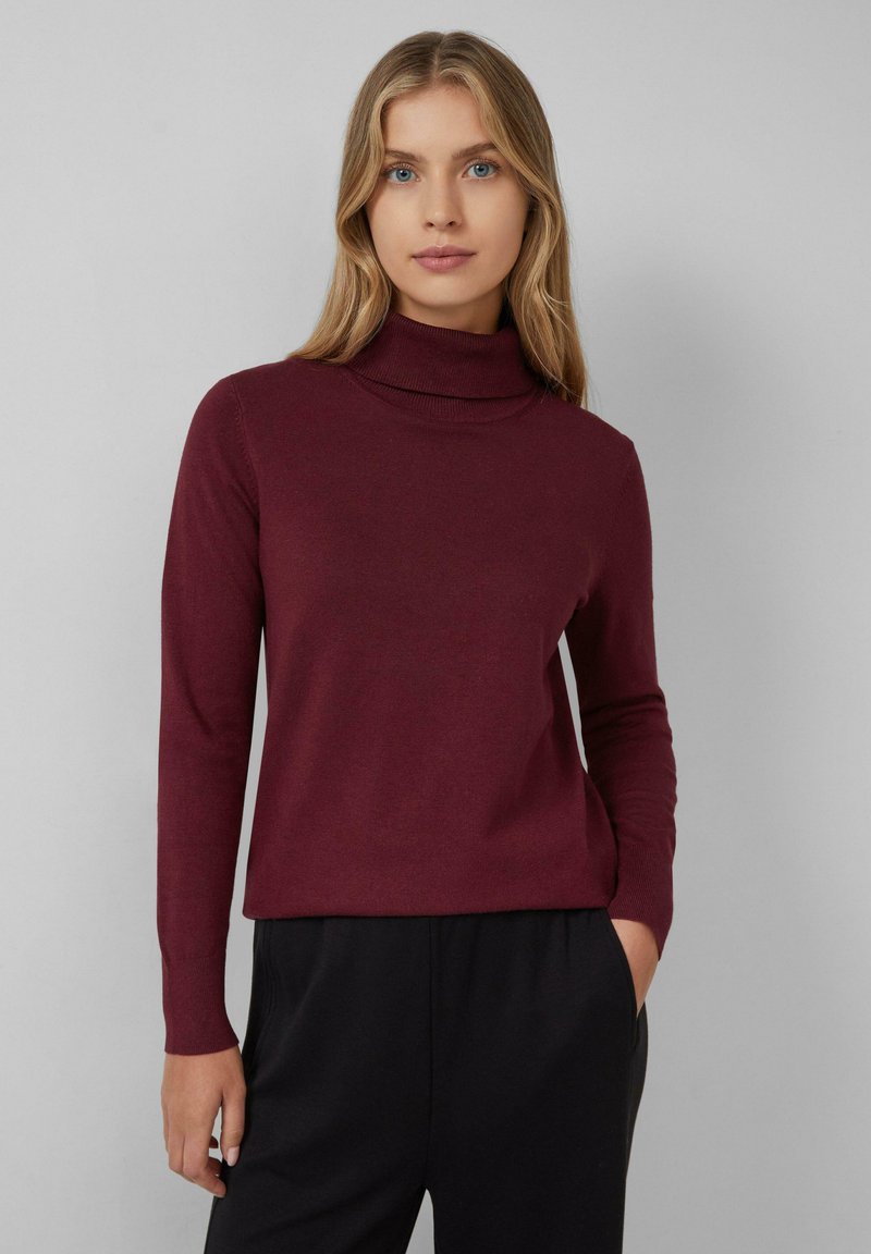 Bordo turtleneck pulover, narejen iz mehkega materiala, z dolgimi rokavi in prilegajočim krojem, v kombinaciji s črnimi hlačami.