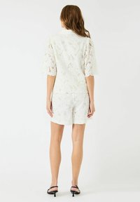 Lace antrekk i hvitt, med en kortermet topp med blomster mønster og matchende shorts. Glatt tekstur og bølgete kanter. Minimalistisk design.
