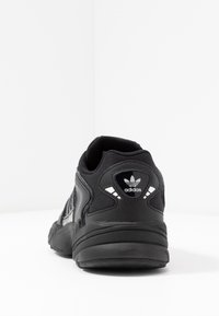 Svart idrottssko med övre del av mesh och syntetiska detaljer. Har en vadderad krage, kontrasterande ränder och en dekorativ logotyp på hälen.