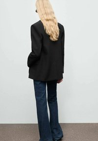 Černý oversized blejzr se strukturovanými rameny, v kombinaci s tmavými rozšířenými džíny. Hladký povrch, minimální detaily, jednoduchý design.