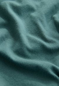 Puuvillakangas tekstuuriga, teal-värvi, millel on pehmed voldid ja kortsud, rõhutades selle sujuvat ja kerget olemust.